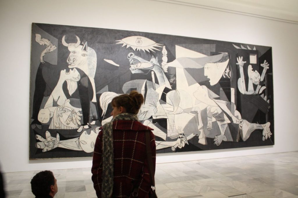 Two visitors stand closely together, looking at Picasso’s Guernica in Madrid’s Museo Reina Sofía, a great place for those solo travelling madrid