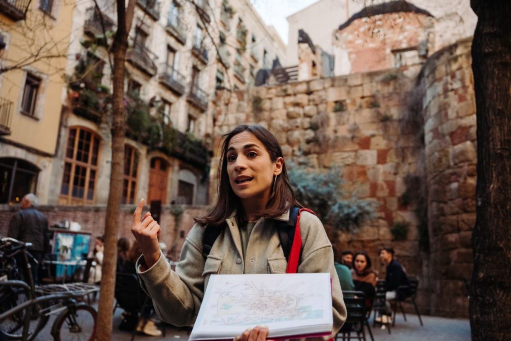 A woman tour guide explaining the history of the city, infront of a gothic quarter building and tapas bars in Barcelona.