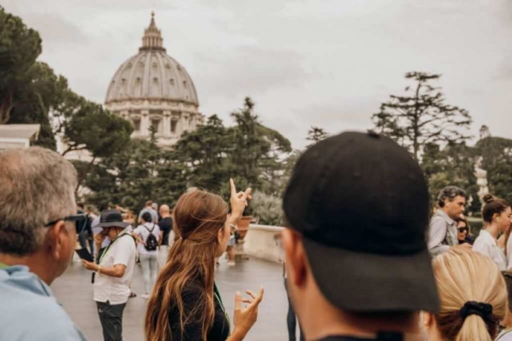 Tourists listen to a guide pointing at St. Peters Basilica dome, Vatican City, amid festive Rome jubilee activities.