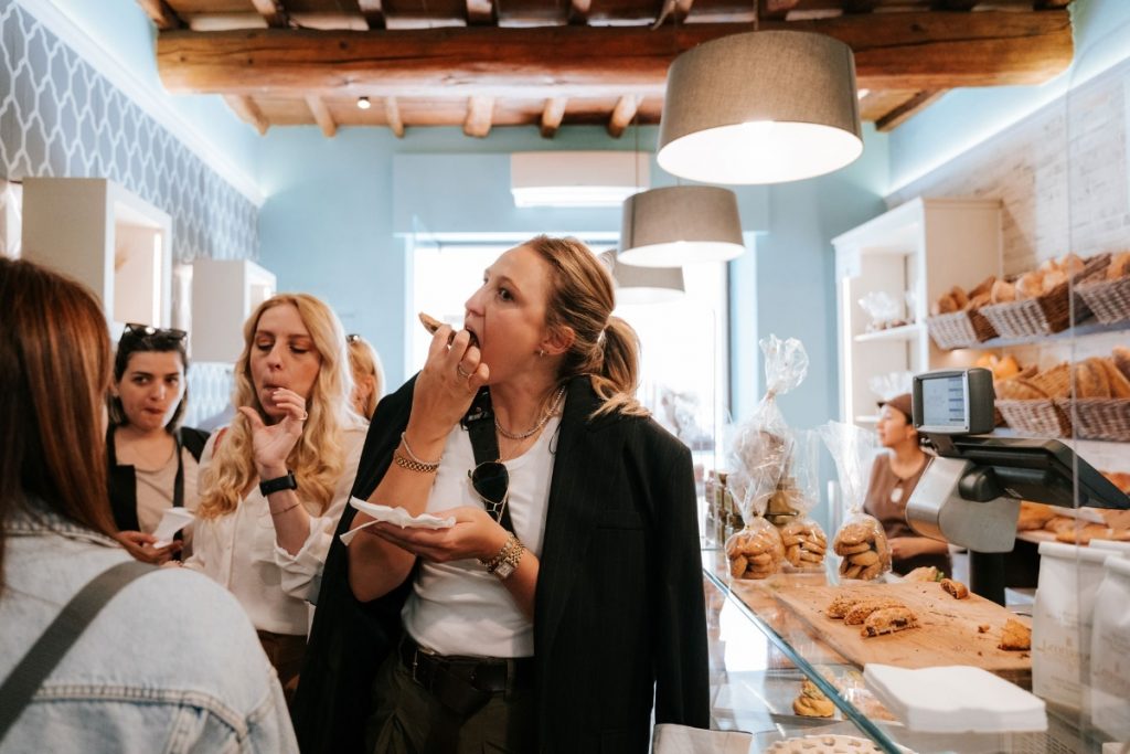 Four women taste pastries inside Forno Ghibellina near SantAmbrogio Market in Florence; shelves display fresh loaves and sweet treats.