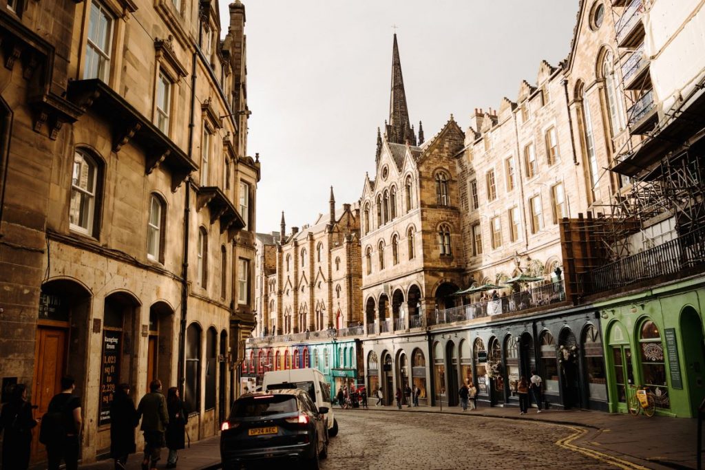 People walk along Victoria Street in Edinburgh, which is lined with historic buildings and colorful shops..