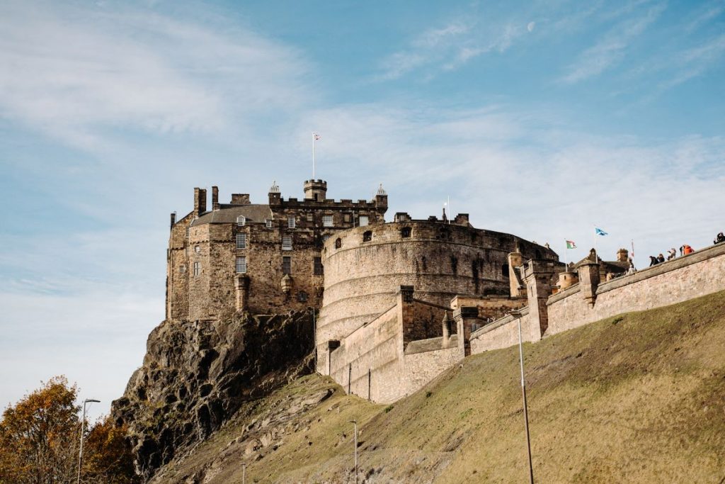 Edinburgh Castle stands on Castle Rock, with visitors exploring its ancient stone walls and Scottish flags waving in the breeze.