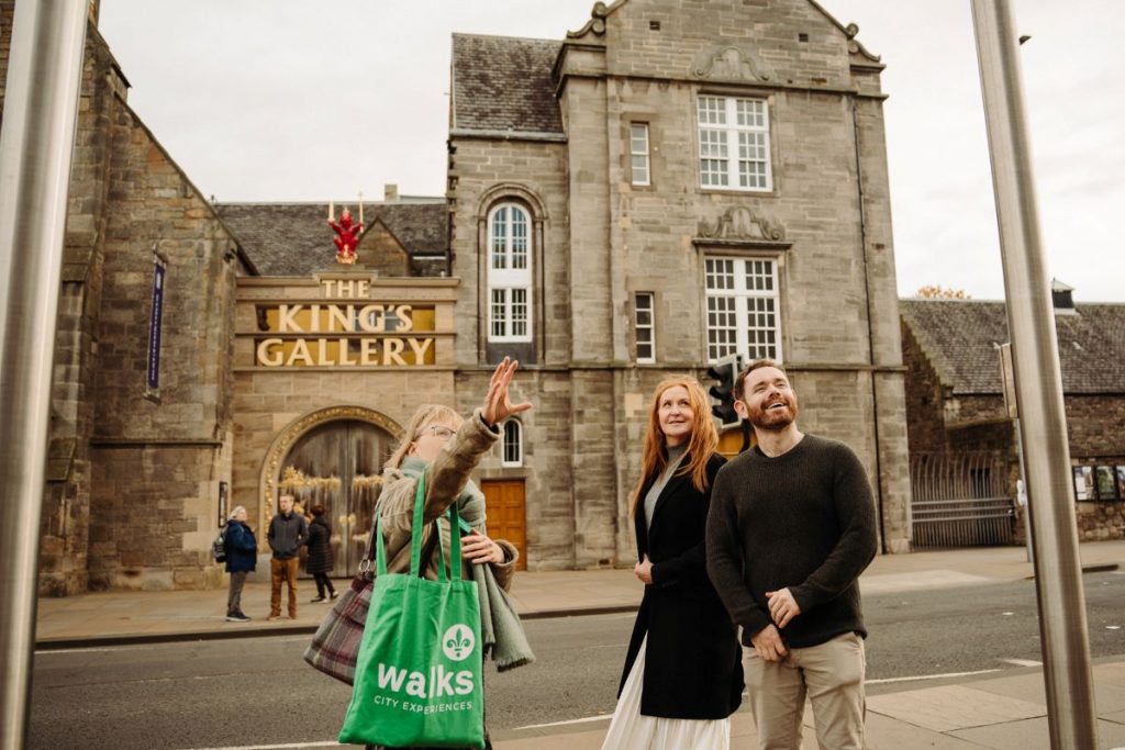 Three friends stand outside The Kings Gallery on the Royal Mile in Edinburgh, with one woman pointing at architectural details above.