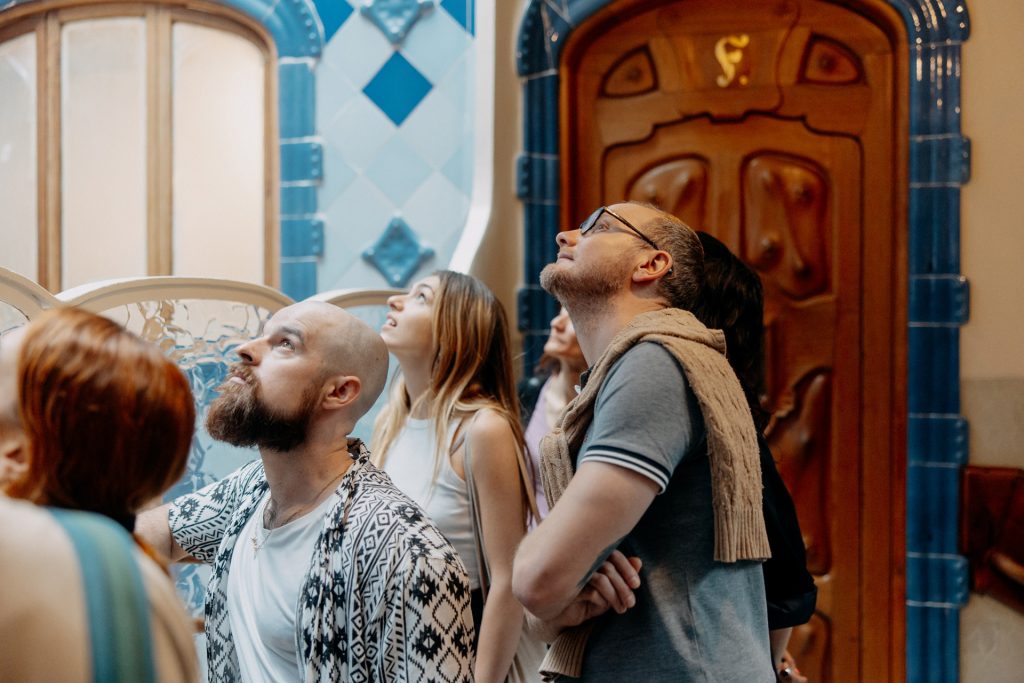 A group of people in a grand, historic hall with blue and wood accents gaze upward, possibly admiring the intricate ceiling inside casa Batllo, Barcelona