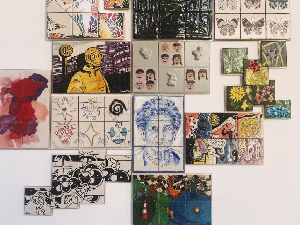 Colorful tiles featuring abstract patterns, faces, animals, and flowers decorate a white wall at the Tile Museum, which is a great activity to do on a solo trip to Portugal