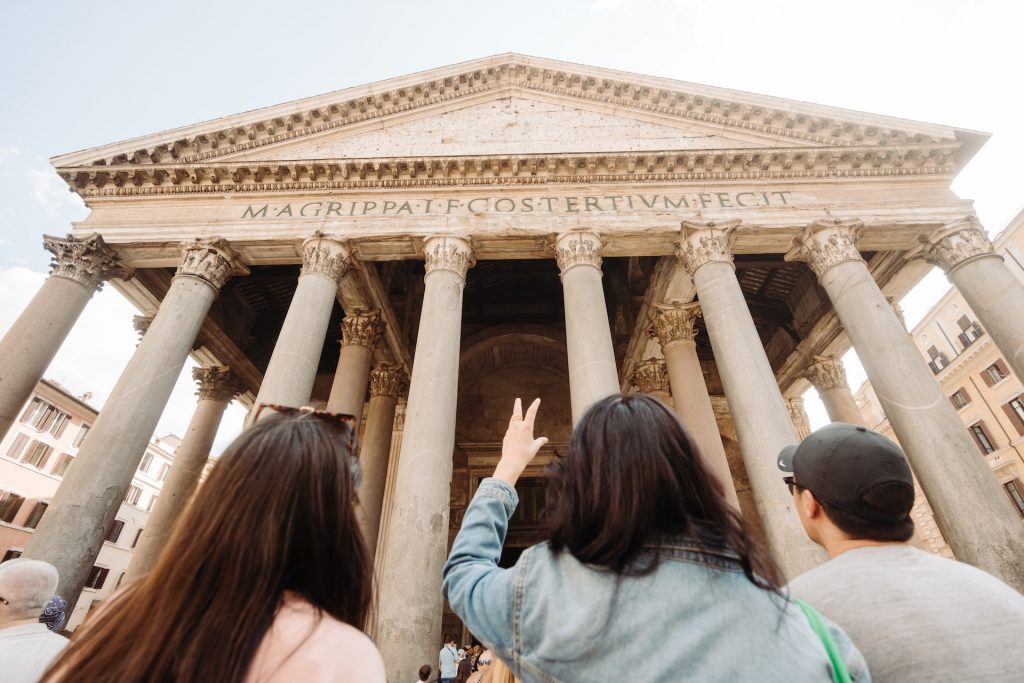 A travel guide and two tourists gaze up at the Pantheon’s grand columns in Rome. The sky is clear and blue. one tip for visiting Rome, do not forget to look up!