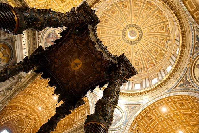 Looking up at St. Peter’s Basilica’s dome, ornate gold detailing and grand columns highlight Vatican City’s rich architectural heritage.