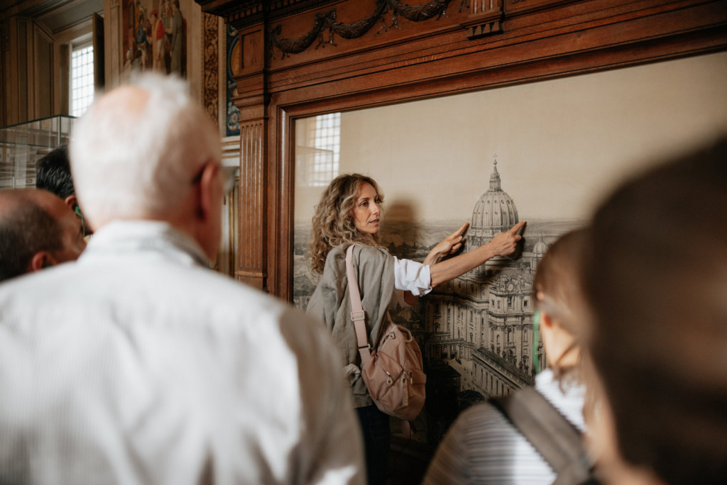 A tour guide leads a group through a museum, pointing at a drawing of St. Peter’s Basilica.