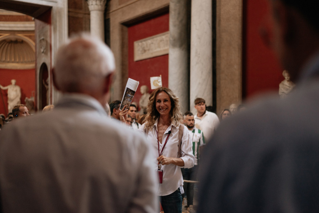 A smiling guide holds a brochure while leading a group through the Vatican Museums in Rome.