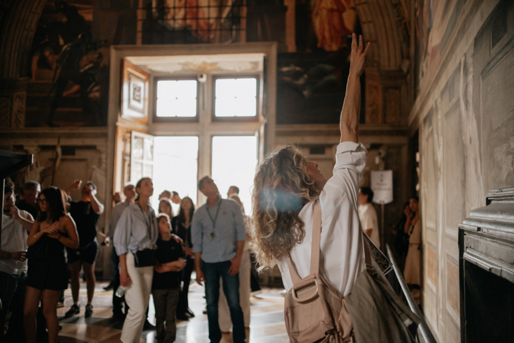 A Sistine Chapel Guide points at Raphael’s School of Athens fresco in the Vatican Museums as visitors view the artwork.